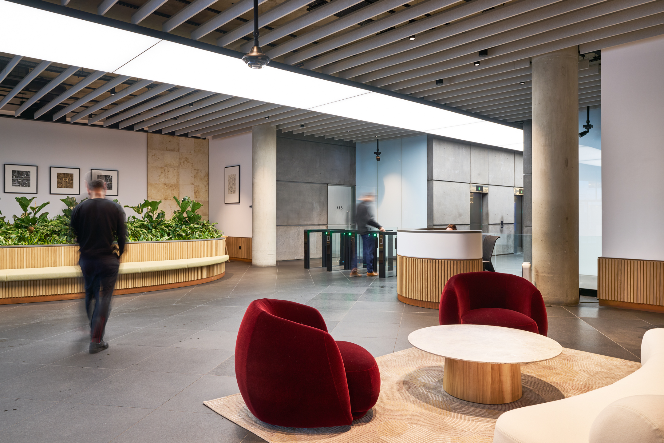 A stylish seating area at 350 Euston Road designed by Modus, where plush red chairs and a wooden coffee table create a comfortable waiting or meeting space. The area is framed by lush plant life and sleek architectural elements, reflecting a modern, welcoming environment.