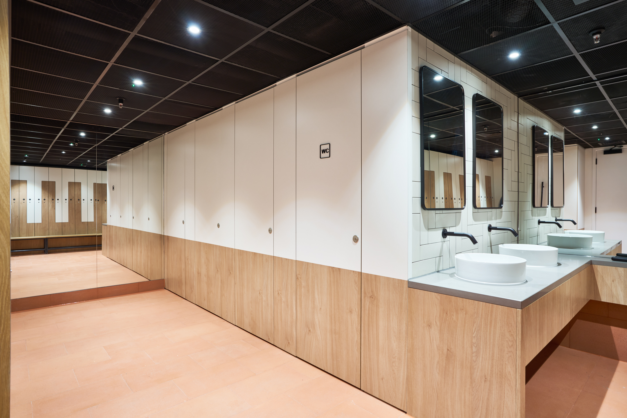 A sophisticated washroom and locker area at 350 Euston Road, featuring wooden lockers and modern wash basins set against a backdrop of mirrors and white tiles. The design by Modus combines functionality with stylish, clean lines to enhance user experience.