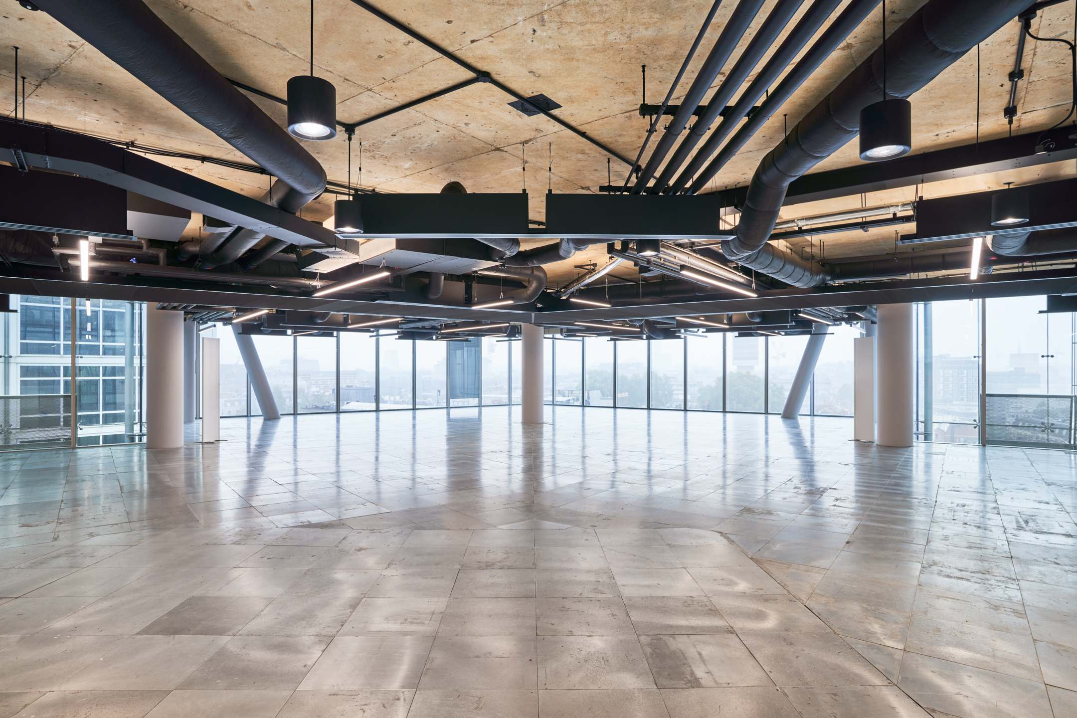 A wide-angle view of a modern, open-plan office space at 350 Euston Road, showcasing a clean design with exposed ductwork and suspended lighting. The floor is tiled with large, reflective tiles, providing a bright and airy feel, indicative of Modus's contemporary style.