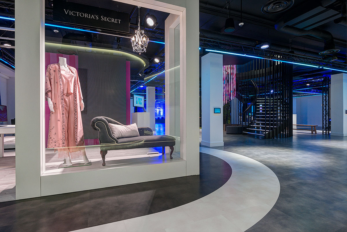 A showroom-style display area at Harman displaying a Victoria’s Secret-themed installation with a mannequin dressed in a pink robe and pyjamas. The space is enhanced by ambient blue lighting.