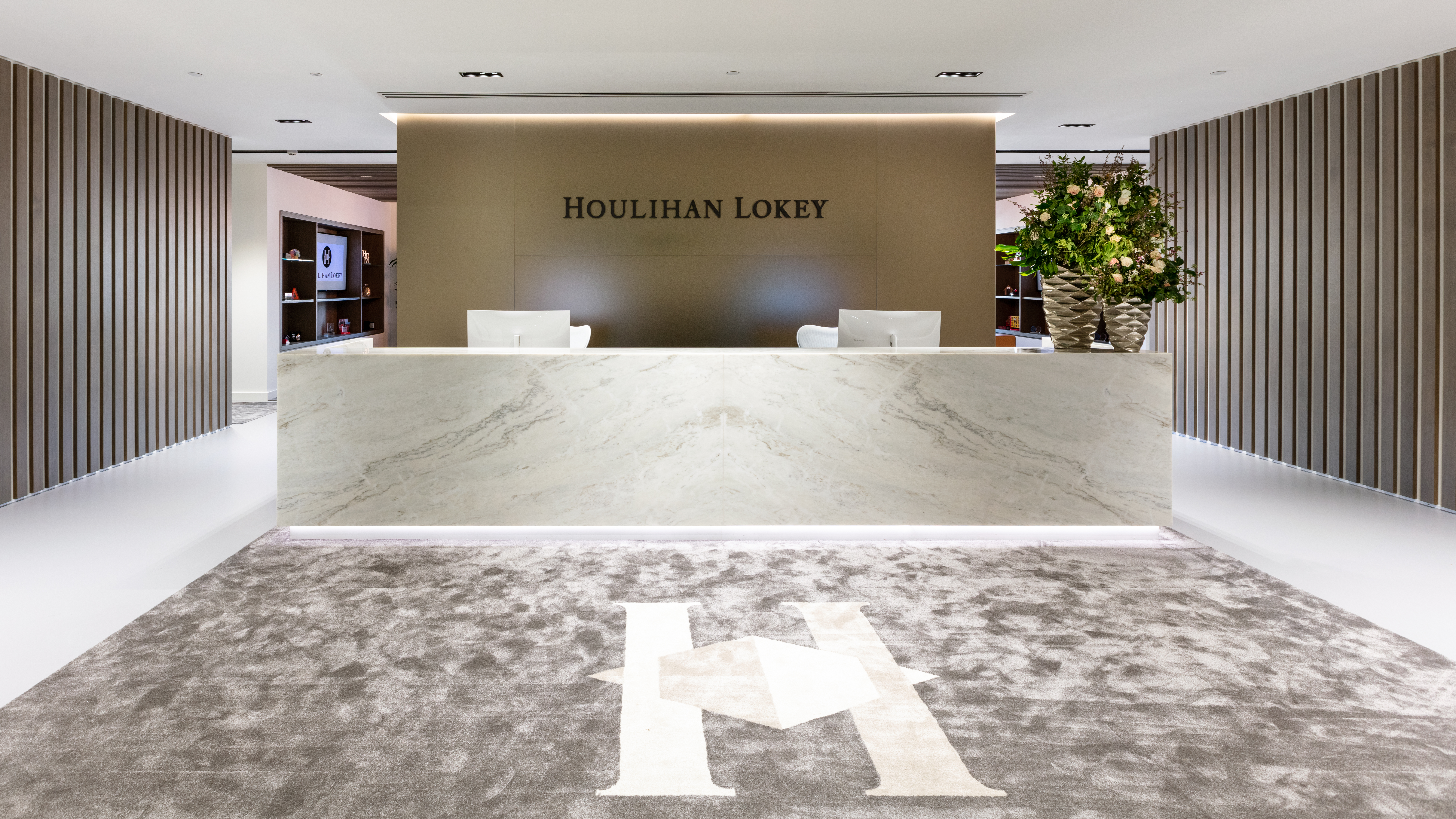 The reception area of Houlihan Lokey features a sleek, modern design with a marble desk and neutral tones, embodying professionalism and elegance. Modus Workspace designed this space with understated luxury, creating a welcoming entrance.