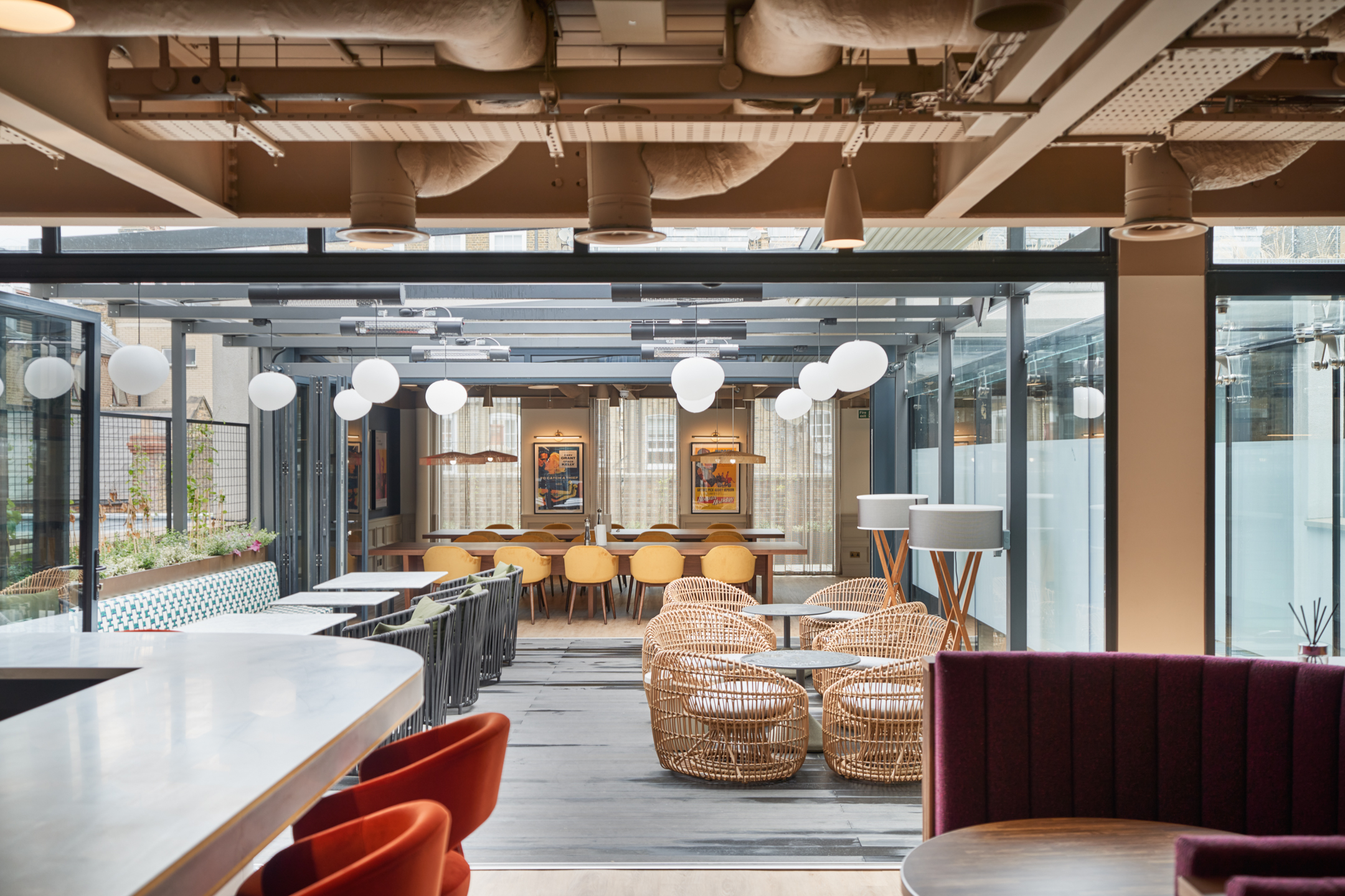 A stylish office dining area at a private equity firm in Marylebone, designed by Modus Workspace. The space features open seating, wicker chairs, and hanging globe lighting, creating a warm and collaborative environment.