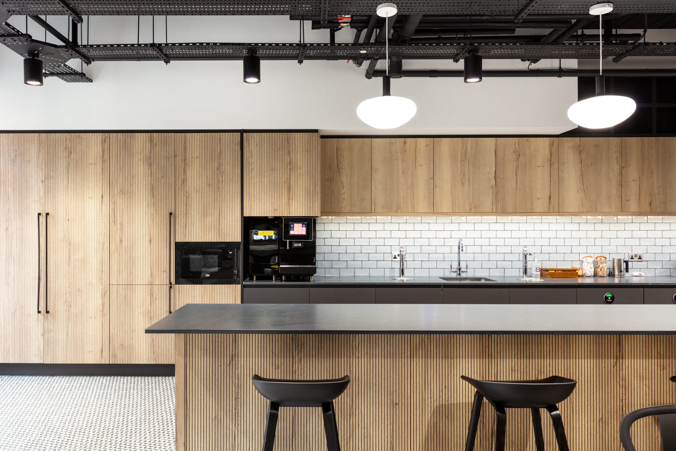 Modern breakout space at Russell Reynolds designed by Modus Workspace features cosy booth seating with a mix of greenery and industrial lighting. The environment is ideal for informal meetings or quick coffee breaks.