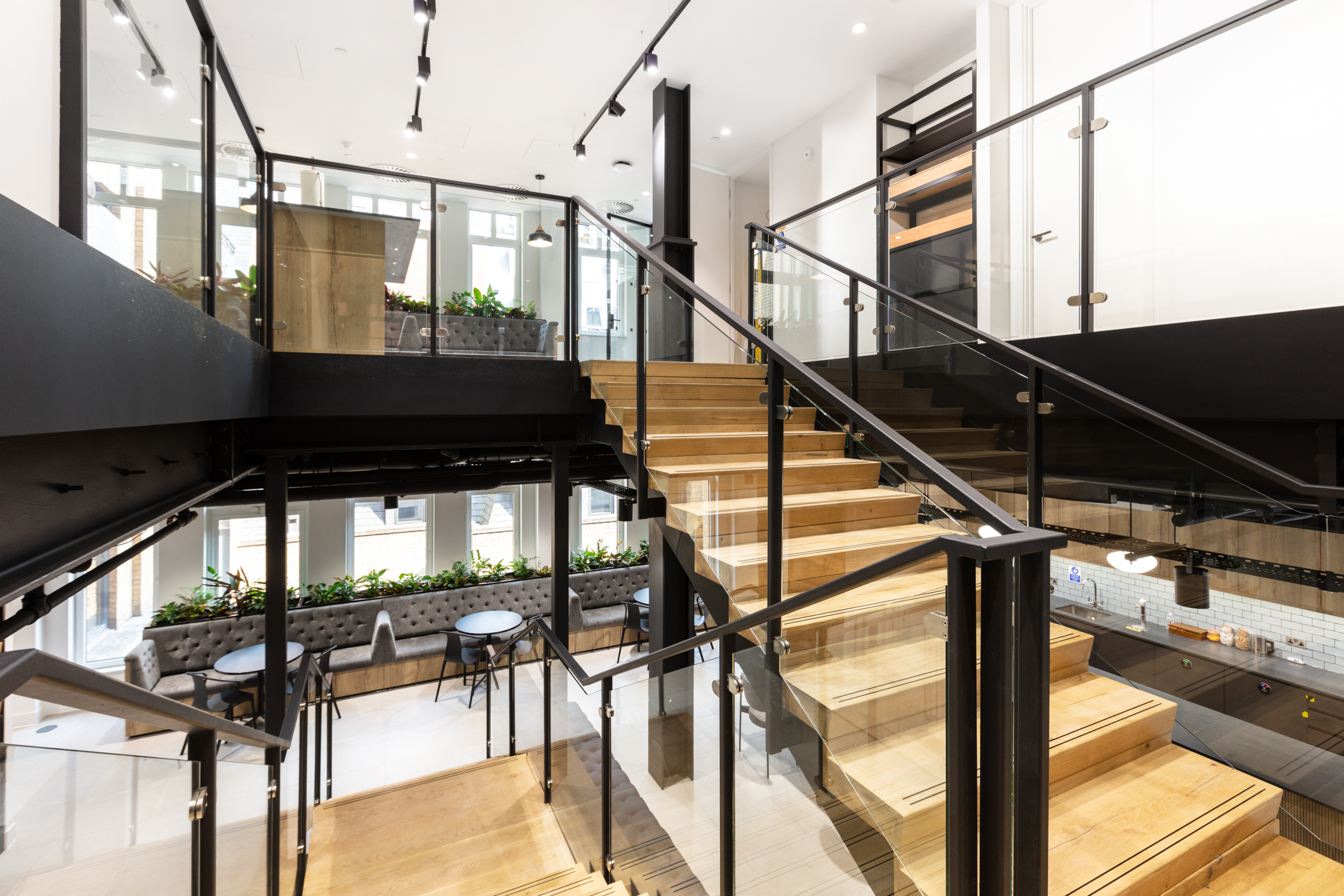 A central staircase connects two levels of the Russell Reynolds office, designed by Modus Workspace. The area also includes comfortable seating near lush indoor plants, creating a welcoming atmosphere for informal conversations or solo work.