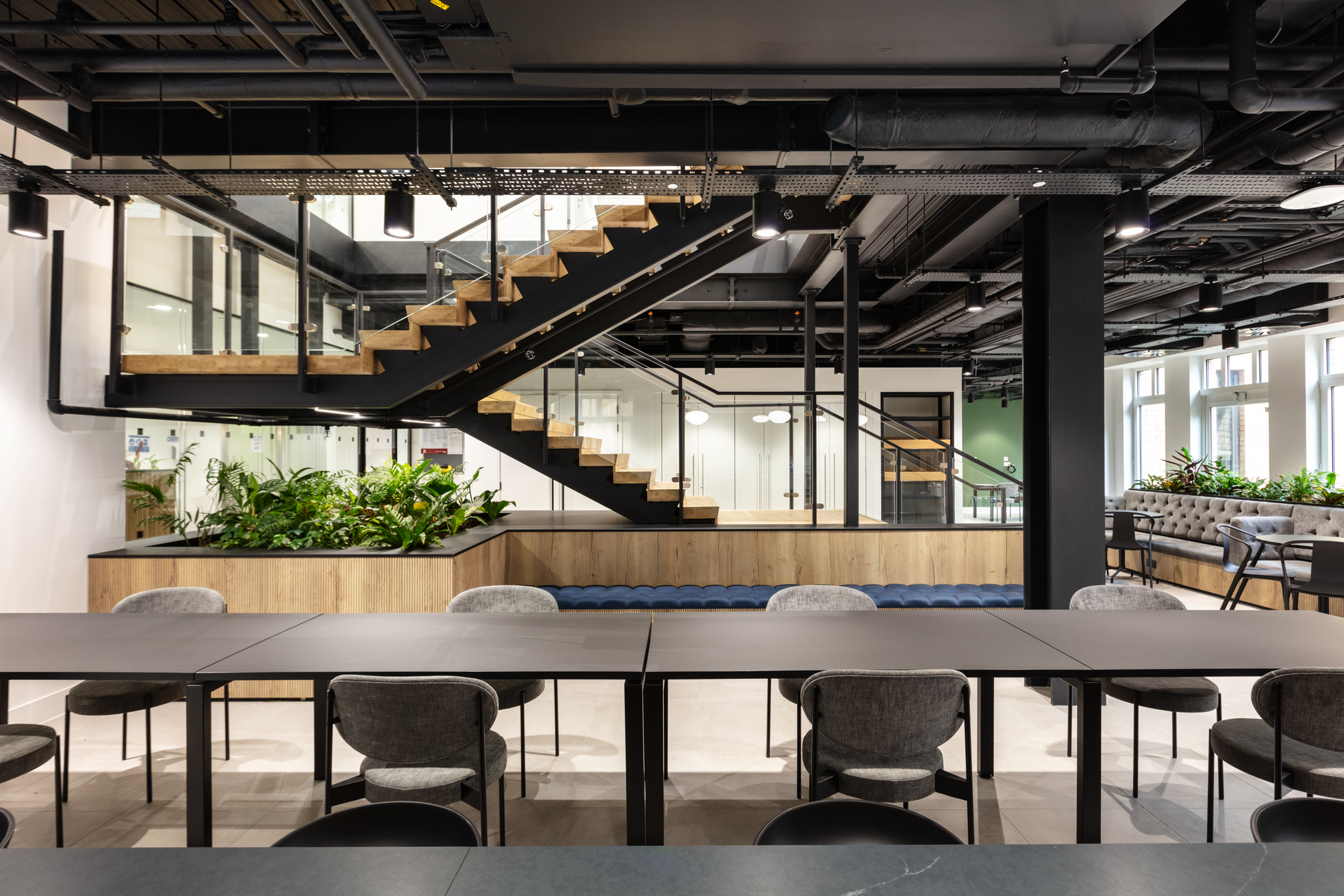 Modern office space for Russell Reynolds, featuring open seating, industrial ceilings, and a striking wooden staircase with greenery.