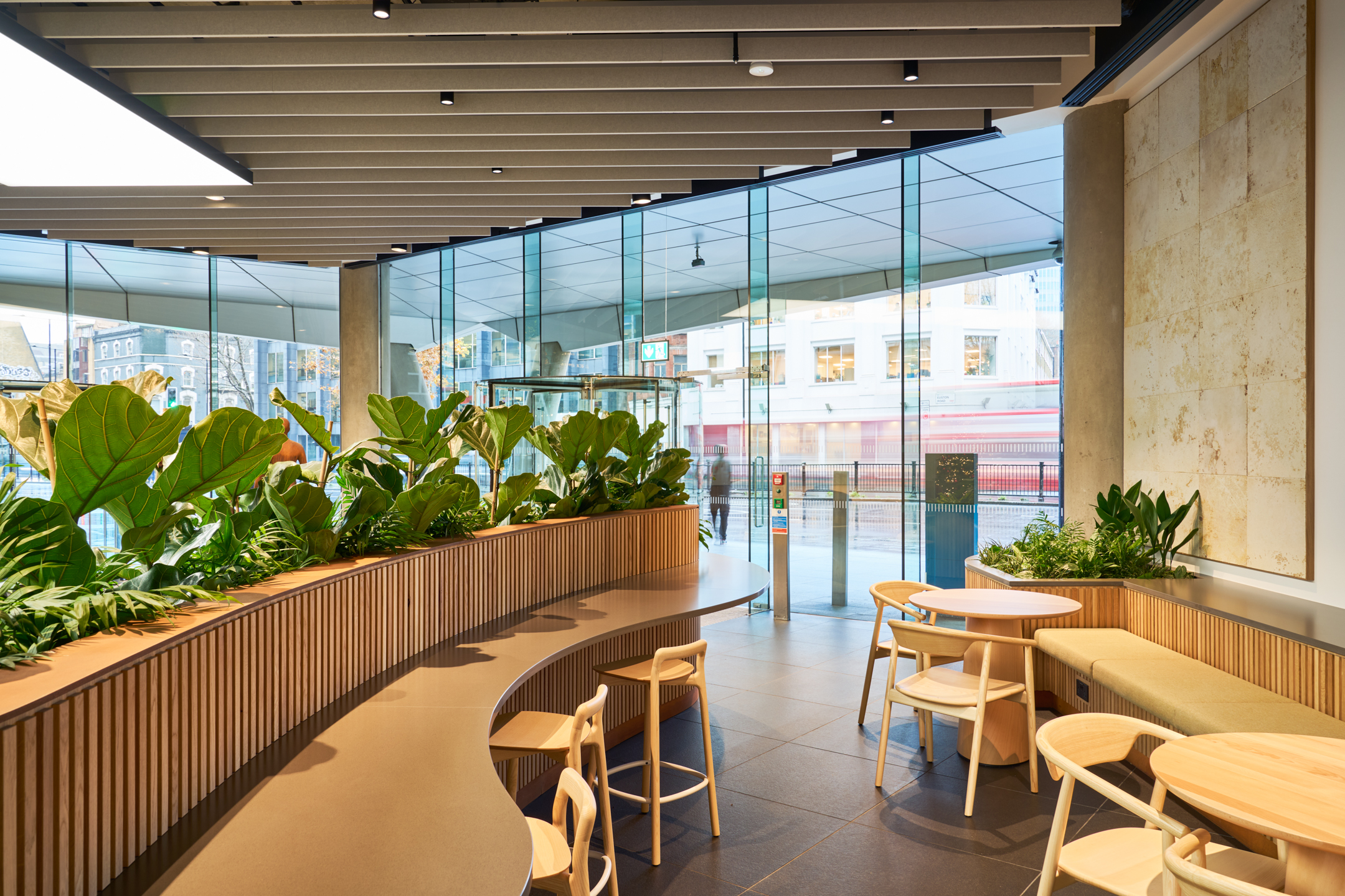 A vibrant, modern office reception with large glass windows and greenery, highlighting sustainable workspace design discussed at FOOTPRINT+ 2024.