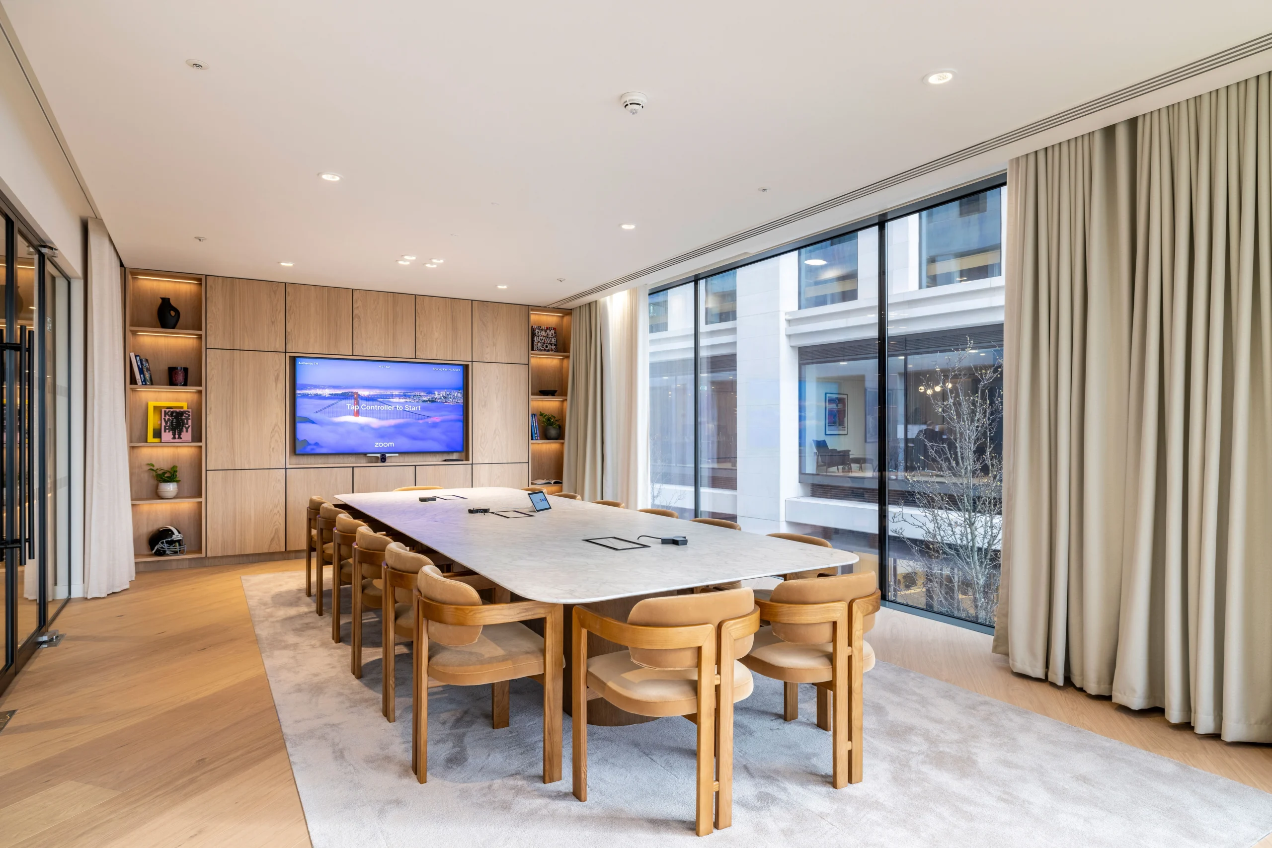 A feature wall at Authentic Brand Group, designed by Modus, displays a collage of black-and-white images of people surrounded by wooden panelling and integrated shelves displaying books and plants.