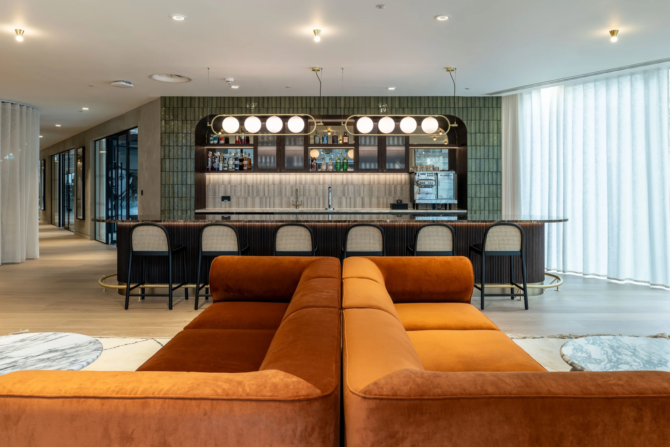 A stylish display area at Authentic Brand Group, designed by Modus, featuring mannequins on a raised platform, velvet green sofas, and glass doors leading to a retail-inspired setting.