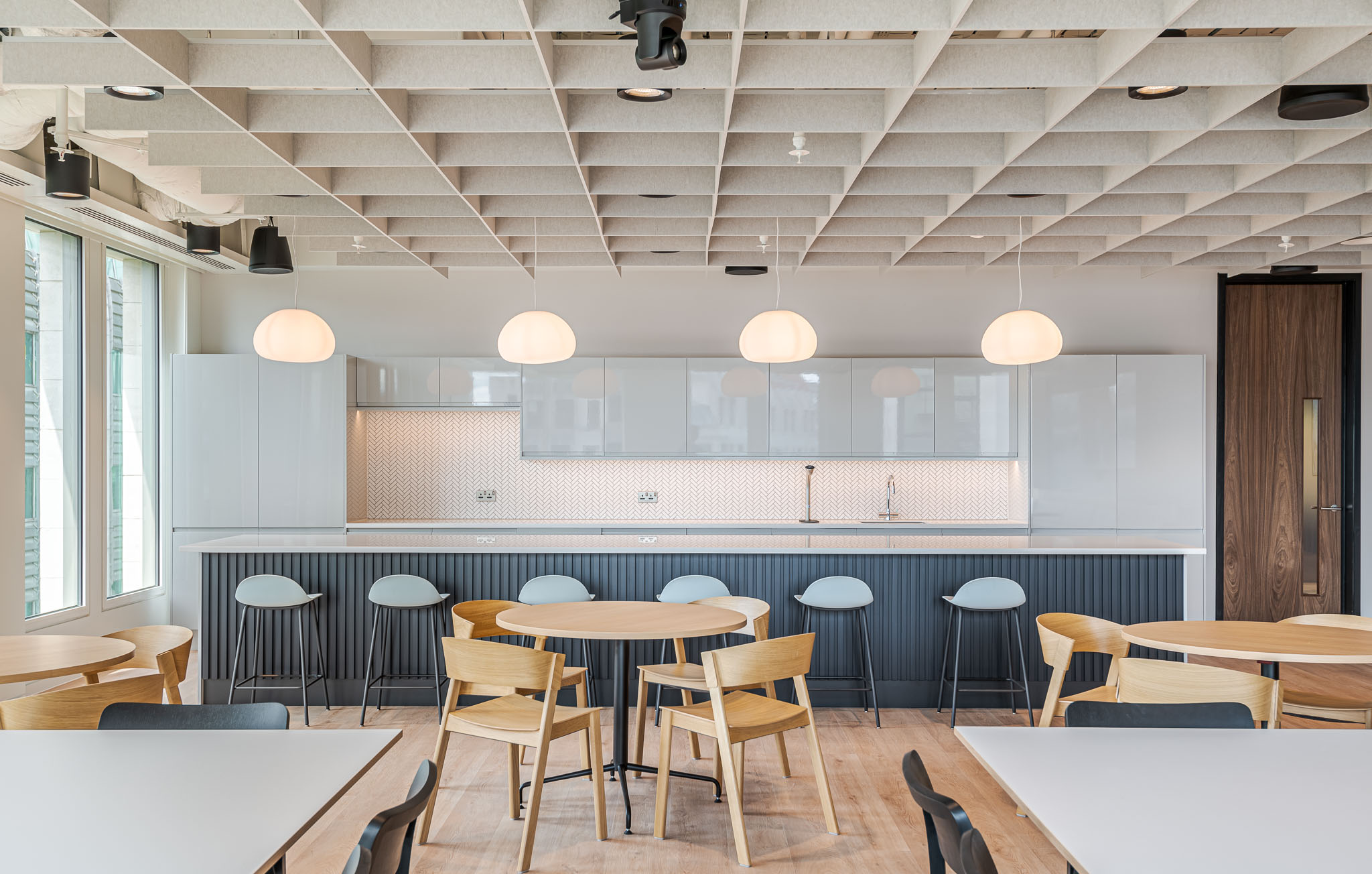 A blue and modern teapoint at the Bank of Ireland, designed by Modus Workspace, equipped with round tables and pendant lighting, creating an inviting break area for employees.