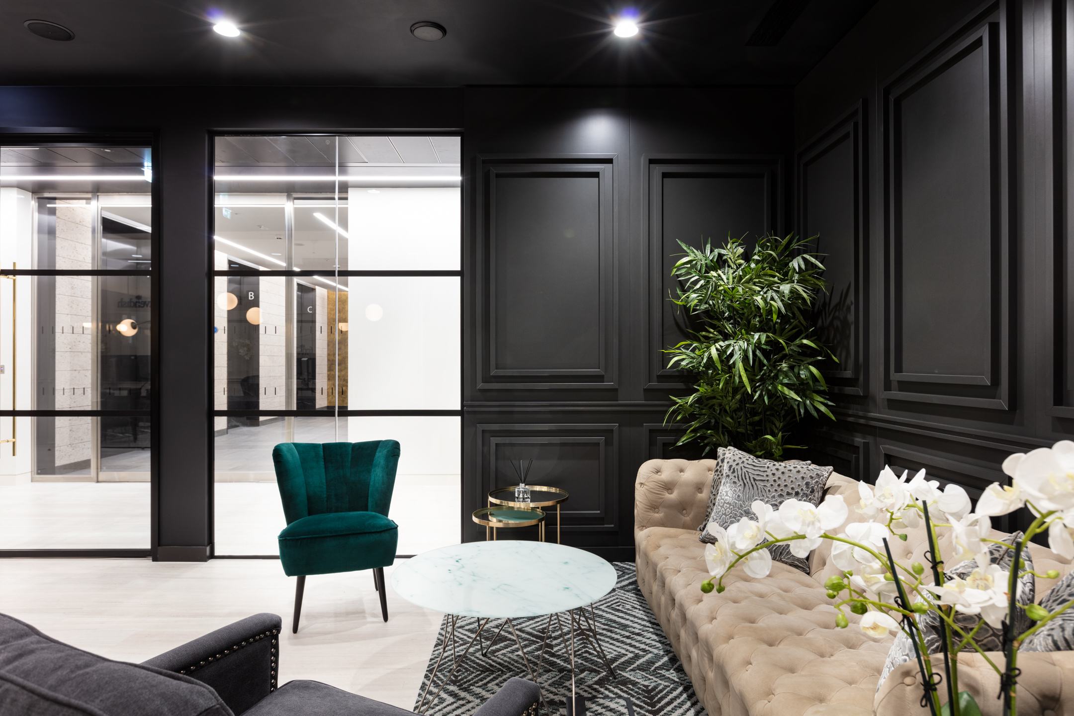 A comfortable seating space at finnCap with a beige sofa, teal velvet chair, and glass tables against dark panelling.