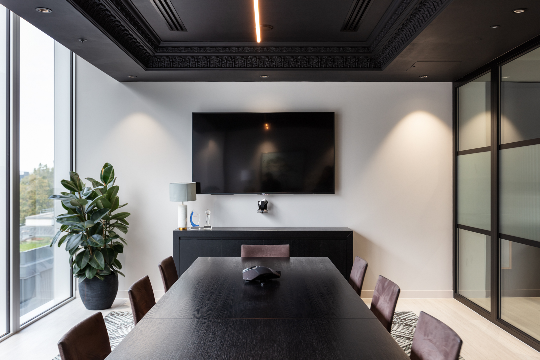 A finnCap meeting room showcasing a sleek black conference table, leather chairs, and a large TV screen, with minimalistic decor and natural light from floor-to-ceiling windows.