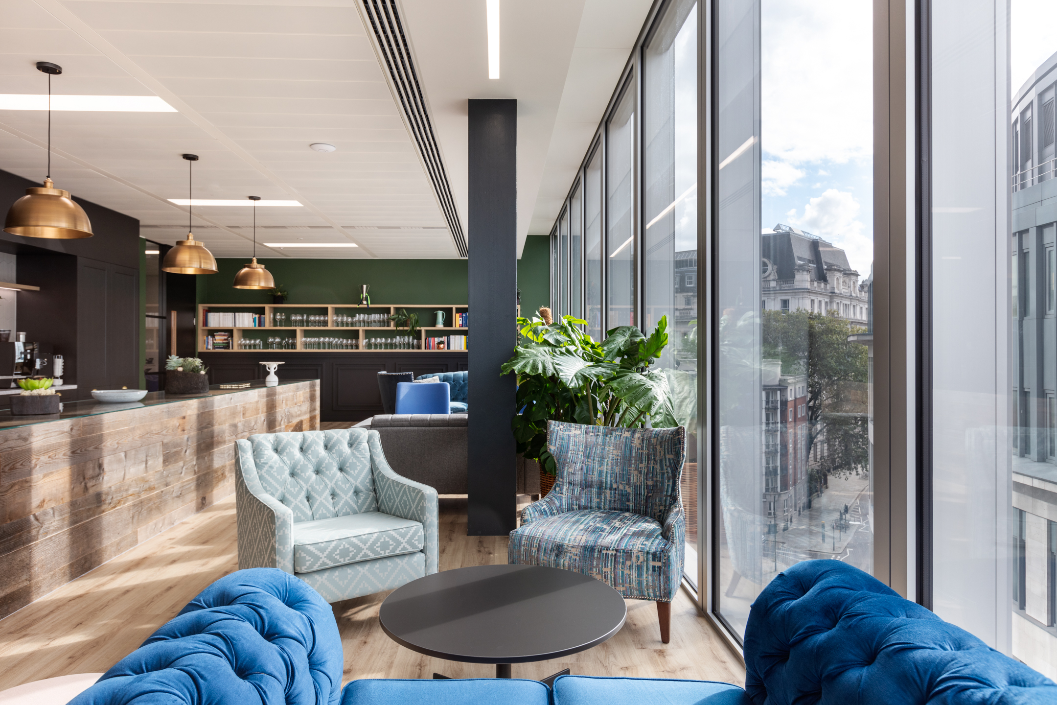 A breakout area in the teapoint at finnCap with plush, brightly coloured seating, large windows, and indoor plants.