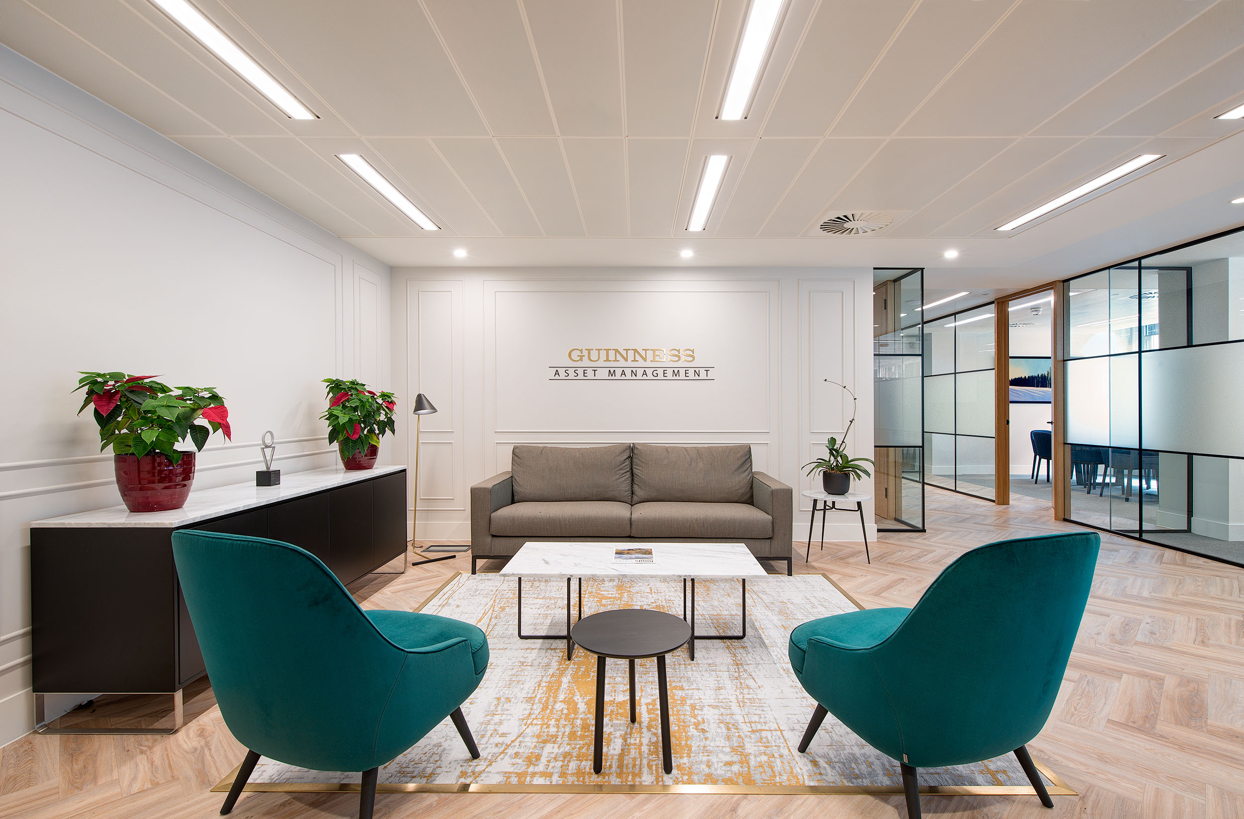 Reception area of Guinness Asset Management designed by Modus Workspace, featuring modern furniture, teal chairs, and elegant décor for a welcoming atmosphere.