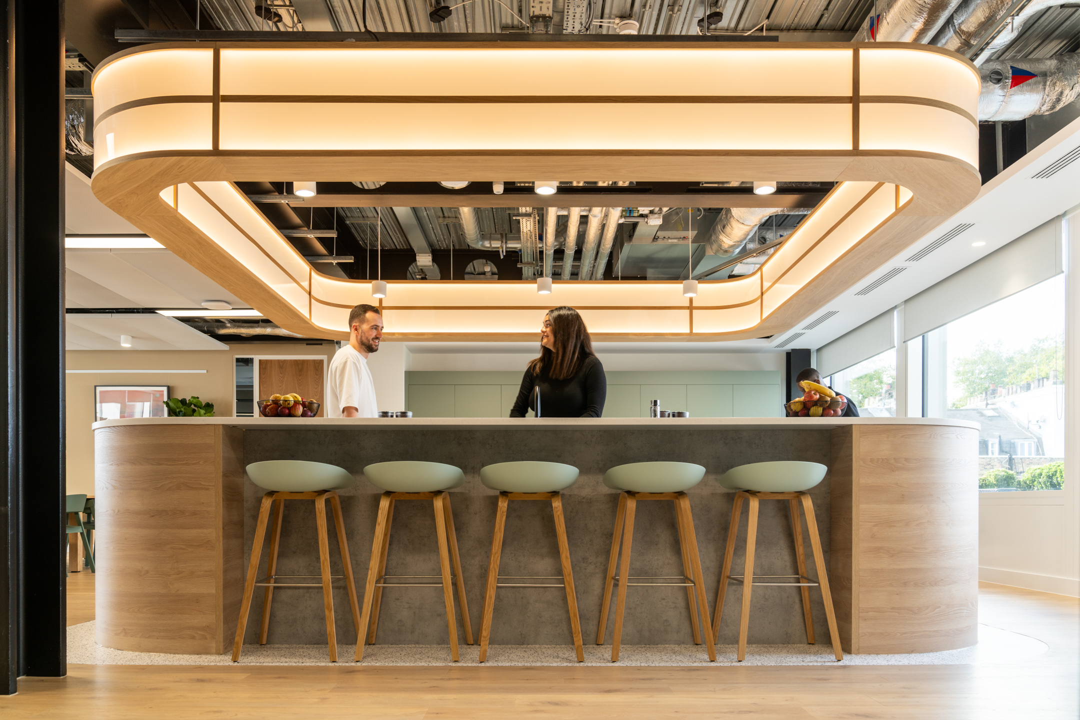 Shionogi kitchen with a curved bar, stools, glowing light fixture, and exposed ceiling.