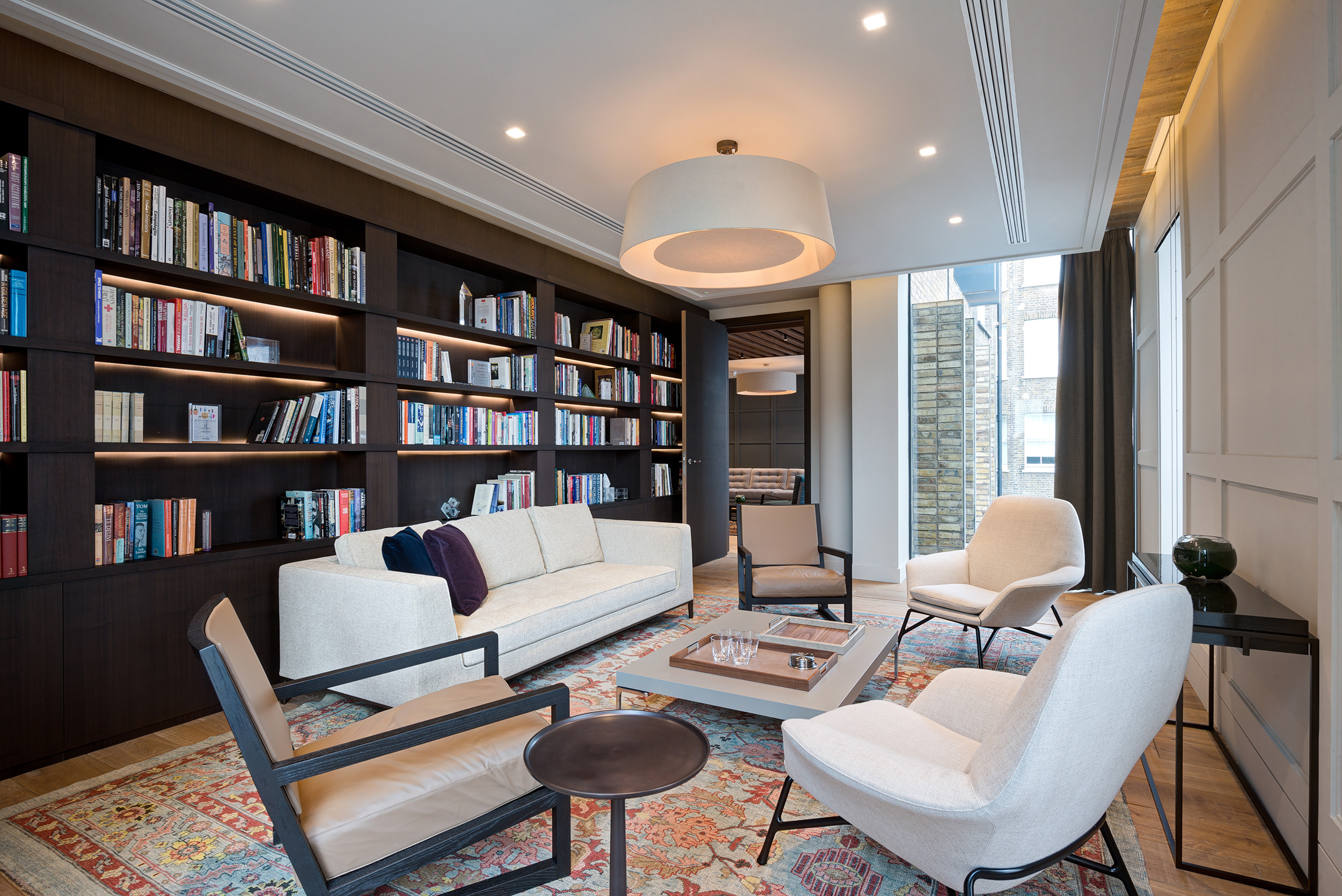 Reading area with built-in dark wood bookshelves, modern lighting, and a seating arrangement with light-coloured furniture at the private equity firm