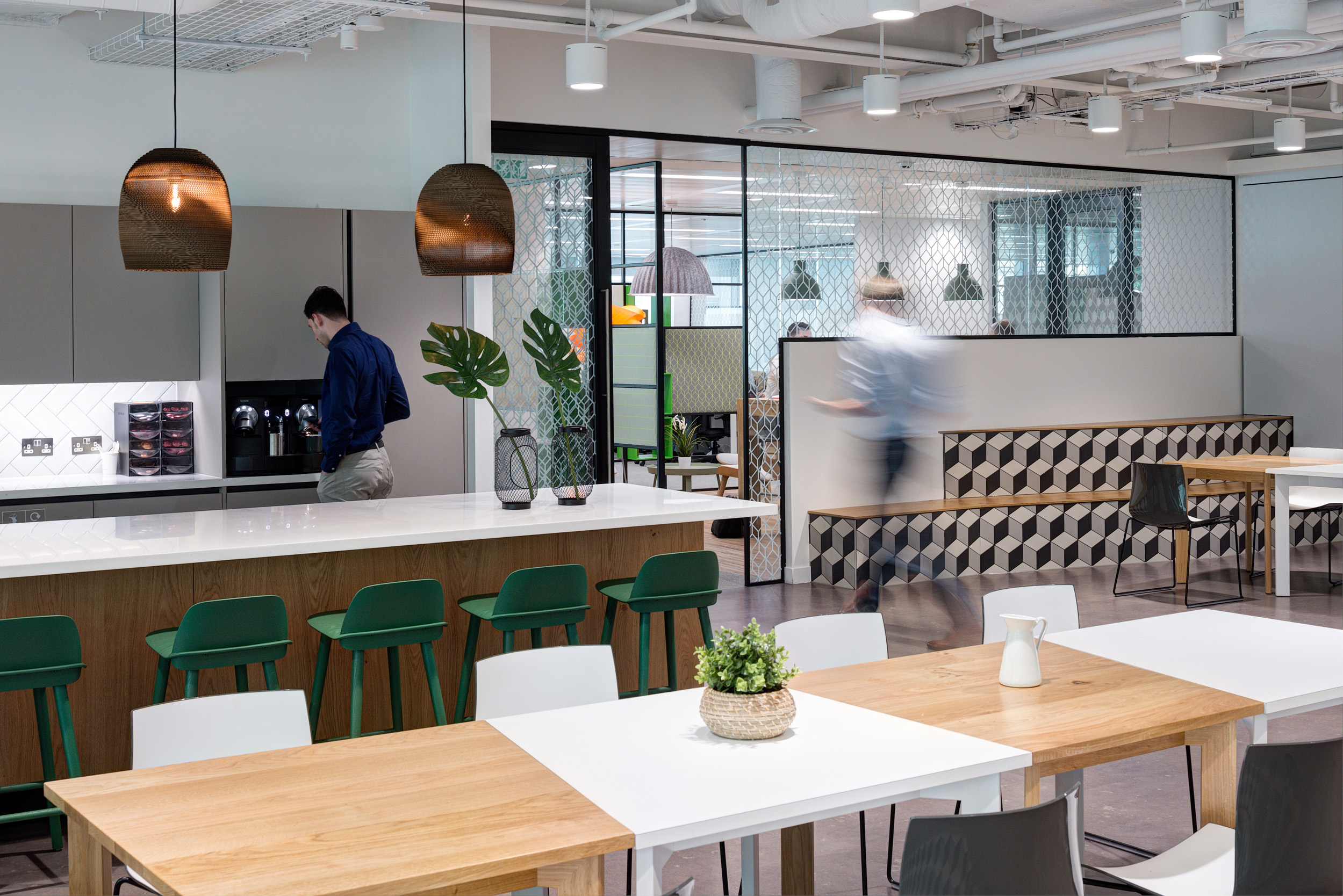 Modern teapoint and breakout area in Reply's office, designed by Modus Workspace. Features green bar stools, wooden tables, and stylish pendant lighting.